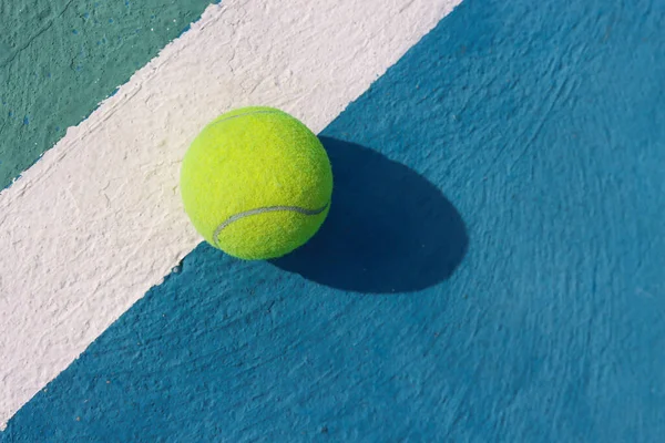 Tennis ball on white line on hard tennis court of blue color. Flat lay, top view, copy space. Summer sport concept. Tennis court with a tennis ball close up. Summer activities and active life