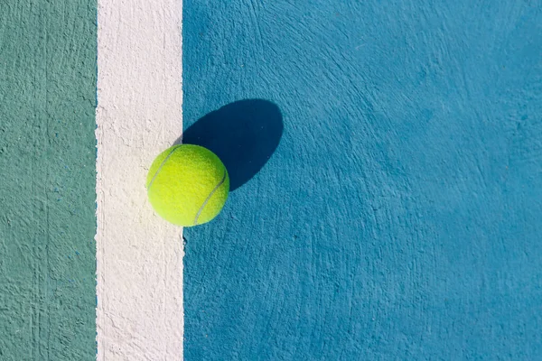 Tennis ball on a white line on hard tennis court of blue color. Flat lay, top view, copy space. Summer sport. Tennis court with a tennis ball close up. Summer activities and active life concept