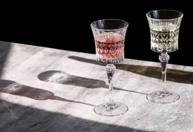 Şampanyalı iki kristal şarap kadehi ve gri arka planda uzun, sert ışıklar ve gölgeli gül şarabı, şarap testi konsepti. Bir restoranda kahvaltı, metin için kopyalama alanı