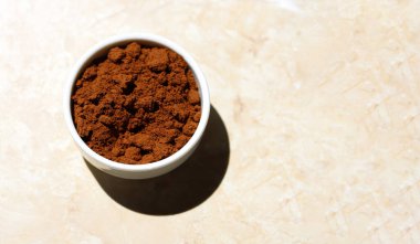 Güneşli bir sabahta açık mermer bir masada kavrulmuş kahveyle seramik beyaz bir kase. Kavrulmuş kahvenin yakın plan fotokopi alanı ile izole edilmiş hafif mermer arka plan.