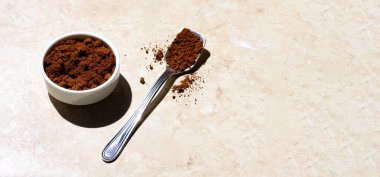 Seramik beyaz bir kase ve güneşli bir sabahta açık mermer bir masada öğütülmüş kahveyle dolu gümüş bir kaşık. Kavrulmuş kahvenin yakın plan fotokopi alanı ile izole edilmiş hali.