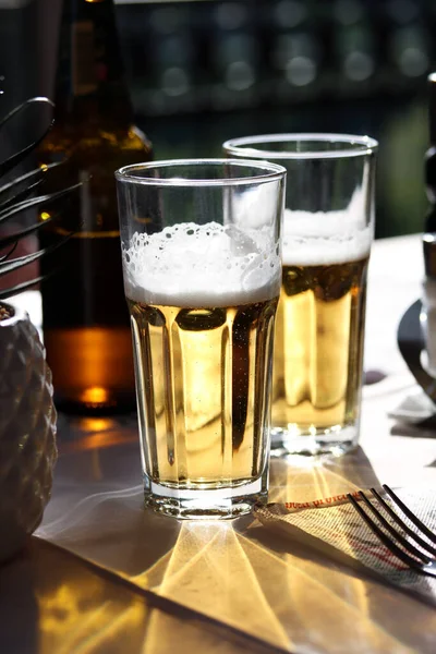 Two glasses of cold light beer with foam on the restaurant table. Real life photography at a restaurant, sunny day, light cold beer on the table, close up.