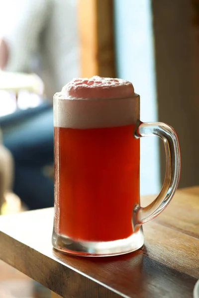 Mug of cold light beer with pomegranate juice and foam on the restaurant table. Real life photography at a restaurant, sunny day, light cold beer on the table, close up.