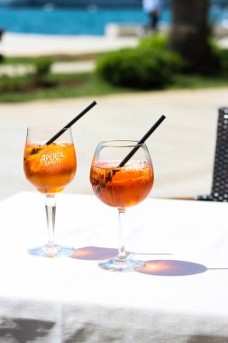 Güneşli bir günde, iki bardak aperol spreyi ve portakal dilimleri ve deniz kıyısındaki bir restoran masasında buz içeren Campari portakal kokteyli. Tatil konsepti. Yaz kokteyli seti, canlı fotoğraf.
