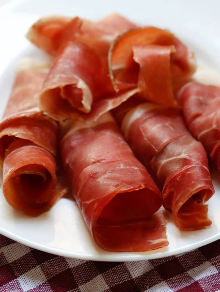 Plate with sliced prosciutto, lifestyle photography. Close up of prsut on white plate, italian or spanish cured meats. Jamon appetizer, brunch time