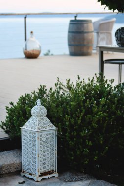 Şık bir şarap imalathanesi. Üzüm bağında saman doğal sandalye ve masalarla şarap tatma alanı, arka planda deniz manzaralı atmosferik bir yer. Şarap degukasyonu için güzel bir şarap restoranı.