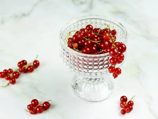 Mermer masada şeffaf kâse içinde taze kırmızı frenk üzümü. Fotokopi aletiyle birlikte açık arkaplanda olgun kırmızı frenk üzümü. Kırmızı üzümlerin minimalist fotoğrafı, seçici odak