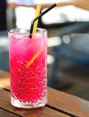 Ahududulu buzlu çay. Limonlu ve buzlu bir bardak ahududu limonatası. Yüksek kristal bardakta soğuk, ferahlatıcı pembe bir kokteyl. Lokanta ahşap masasında. Arka planda bulanıklık var.