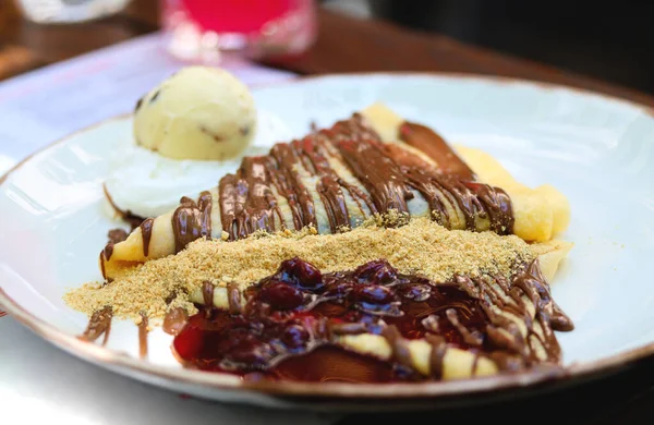 Crepes with chocolate cream. Pancakes with chocolate paste, hazelnuts, cherry sauce and a scoop of ice cream on a white plate on a restaurant table. Thin pancake with chocolate cream