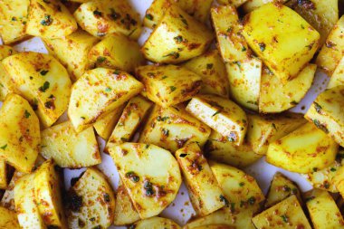 Baharatlı çiğ patates dilimleri. Pişirilmeye ya da kızartılmaya hazır baharat ve otlarla karıştırılmış taze patates parçaları. Pişirilmeye hazır baharatlı çiğ patates.