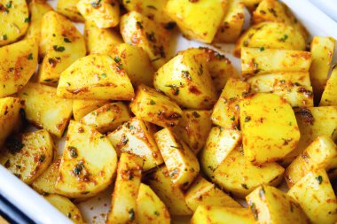 Fırınlanmaya ya da kızartılmaya hazır baharatlı çiğ patates dilimleri. Yabani otlar ve baharatlarla karıştırılmış taze patates parçaları. Pişirilmeye hazır baharatlı çiğ patates.