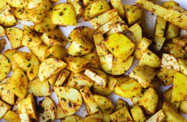 Baharatlı çiğ patates dilimleri, üst manzara, yakın çekim. Fırınlanmaya ya da kızartılmaya hazır baharat ve otlarla karıştırılmış taze patates parçaları. Pişirilmeye hazır baharatlı çiğ patates.