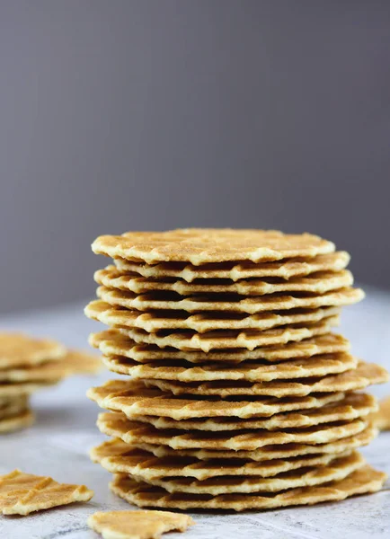 Fotokopi alanı olan gri bir zemin üzerinde bir yığın tereyağlı waffle kurabiyesi, seçici odaklanma. Waffle cipsleri yakın plan. Lezzetli ev yapımı ince waffle, dikey görüntü