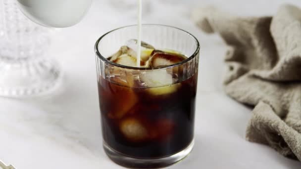 黒いコーヒーを氷のキューブで満たされたガラスに注ぐ アイスコーヒーカクテルを準備する 冷たい爽やかなコーヒーを飲むこと 茶色の飲み物を氷で波形のガラスに注ぐことの近く — ストック動画