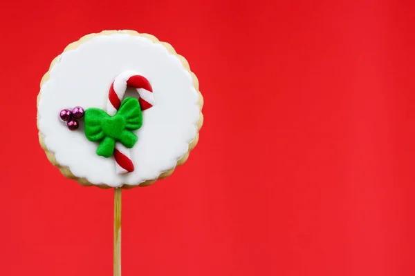 Striking candy cane cookie pop with a green bow over vibrant red background, free space for text. The essence of holiday sweetness, candy cane cookie pop against a red background evokes festive cheer.