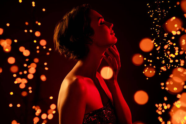 Adorable dreamy lady enjoying fairy time newyear night stand in bright place among garlands illumination.