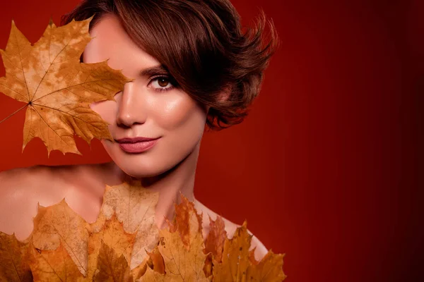 Photo of chic lady cover face with yellow maple leave new lotion extract for smooth facial skin on red background.