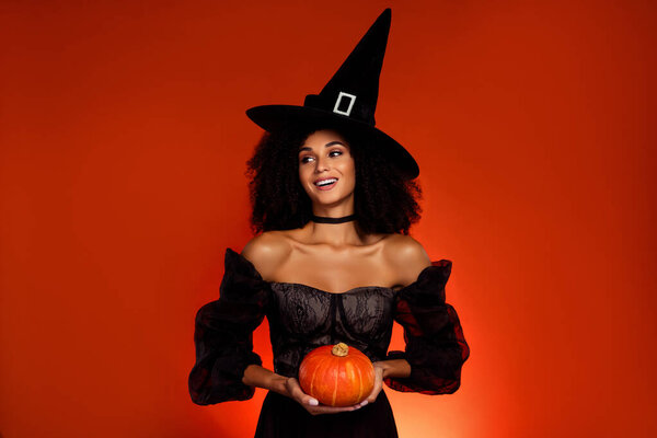 Photo of happy charming witch lady doing incantation sorcery spell using pumpkin over hell color background.
