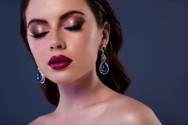 Gri arka planda izole edilmiş lüks butik küpelerin reklamını yapan bir kadın gözlerini kapadı..