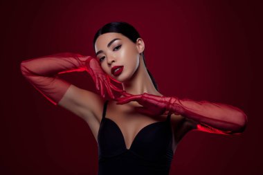 Muhteşem Asyalı genç bayan baştan çıkarıcı dokunmatik yüz eldiveni omuzları izole edilmiş koyu kırmızı arka plan..