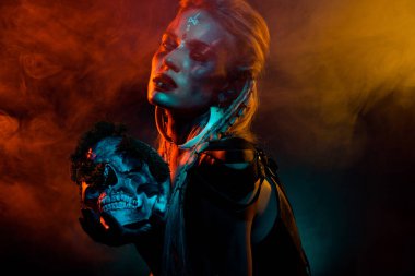 Photo of wild attractive woman wear gothic valkyrie costume holding dead human scull isolated orange fog background. clipart