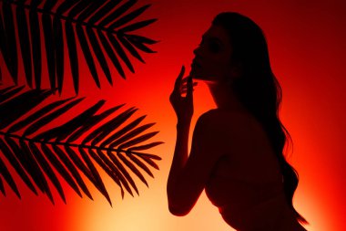 Kadın siluetinin egzotik lagün cennetinde vücut losyonu sürerken fotoğrafı kırmızı sarı güneş renklerine temas ediyor..