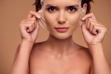 Kadının fotoğrafı. Pastel arkaplan üzerinde saf ipek deriyi kontrol etmek için yüz maskesi çıkarın..