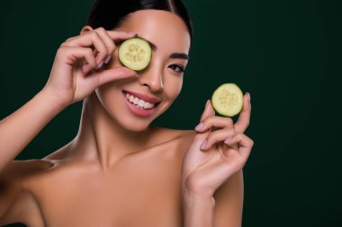 Çekici Asyalı kadının fotoğrafı göz kapağı salatalık dilimi spa salonunun omuzlarını koyu yeşil arka plandan ayırıyor..