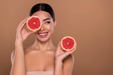 Bayan portresi, greyfurtun yarısını tutun, hijyen zevkini çıkarın, bej rengi arka planda izole edilmiş boş bir alana bakın..