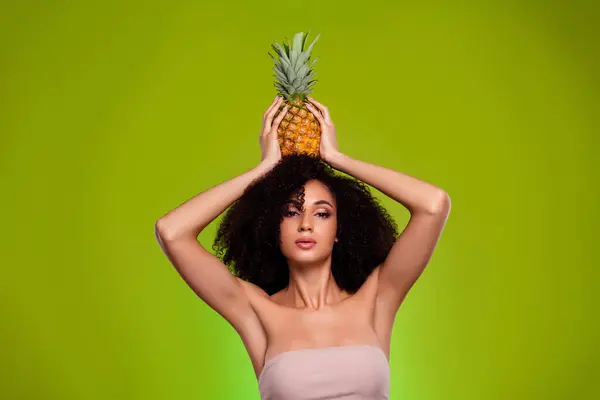 Photo of aesthetic ideal girl with ananas head applying haircare product with exotic dieting ingredient.