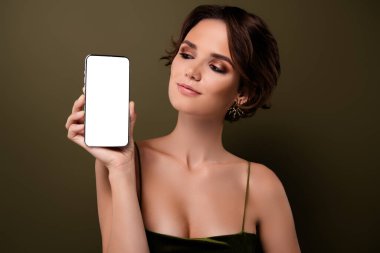 Şık, çekici bir kızın yeşil arka planda izole edilmiş akıllı telefon cihazını gösteren fotoğrafı.