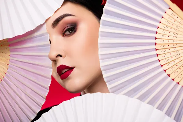 Photo of stunning lovely asian lady theater actress geisha covered face folding fan isolated on red color background.