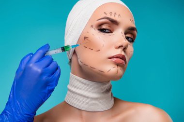 Photo of lady patient doctor hands in blue medical gloves make injection with collagen over cyan color background.
