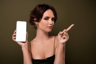 Photo of chic girl hold cell smart phone device demonstrate with finger offer on green empty space background.