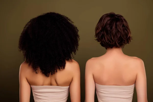 Rear view of two different ladies with curly american hairstyle vs bob brown haircut isolated on khaki color background.