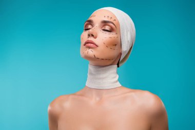 Plastik cerrahi hastası bayanın fotoğrafında tıbbi bandaj izleri var. Cyan arka planda gözleri kapalı..