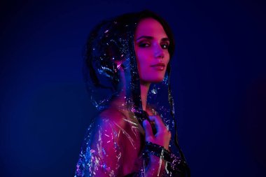 Çekici bir bayanın fotoğrafı şeffaf ceket giyer, su geçirmez başlık giyer ve renkli arka planda izole olur..