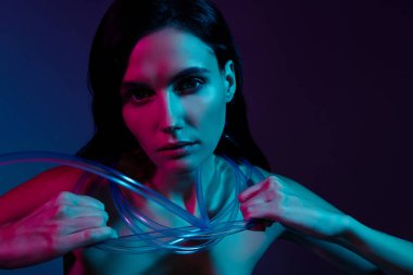 Boynuna plastik kablolar bağlanmış bir kadının fotoğrafı. El ele tutuşmuş. Koyu neon rengi arka planda yok etmeye çalış..
