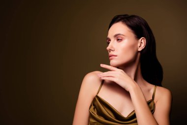 Kahverengi renk arka planında izole edilmiş, fotoğraf stüdyosunda poz veren, ipek haki elbiseli zarif bir bayan..