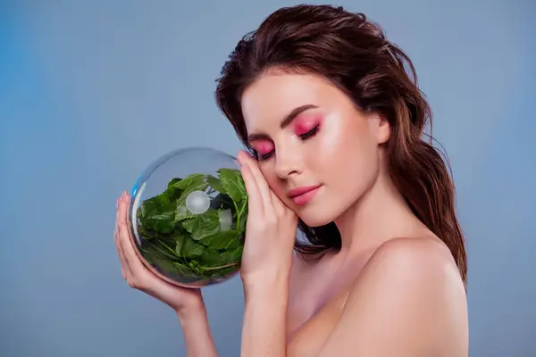 女子手持玻璃球的照片 绿色植物触摸面颊紧闭的眼睛 隔离的灰色背景 — 图库照片