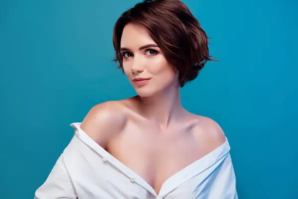 Photo of dreamy bob brown hair model with bare shoulders wearing white shirt isolated on blue color background.