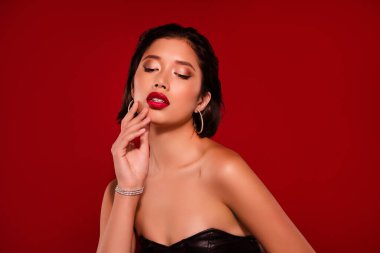 Çekici Çinli genç kadının fotoğrafı yumuşak yüzlü, kırmızı arka planda izole edilmiş siyah deri kıyafetler giyiyor..