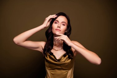 Kahverengi eğimli arka planda poz veren, ipek haki renkli elbiseler giyen büyüleyici, alımlı bir kadının fotoğrafı..