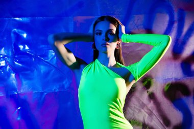 Kendine güvenen model kız kollarının portresi parlak neon ışıklı stüdyo posterinin arka planına dokunuyor..