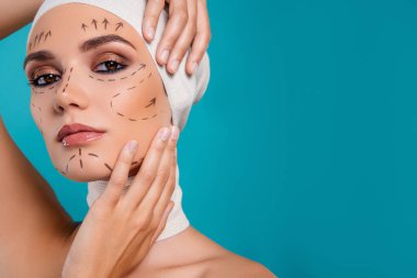 Kadın dokunuş yüz muayenesi fotoğrafı. Plastik cerrahi için hazırlan. Cyan rengi arka planda izole edilmiş..