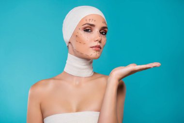Bandajlı kadın fotoğrafı ve düzeltme işaretleri. Cyan arka planda plastik cerrahi el hareketi reklamı..