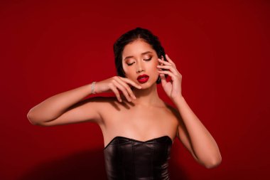 Güzel Japon genç kızın fotoğrafı narin tene dokunuyor. Kırmızı arka planda izole siyah deri elbise giyiyor..