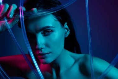 Plastik güzellik kablosuna dokunan kadının fotoğrafı. Kamera ultraviyole neon arkaplanda izole edilmiş..
