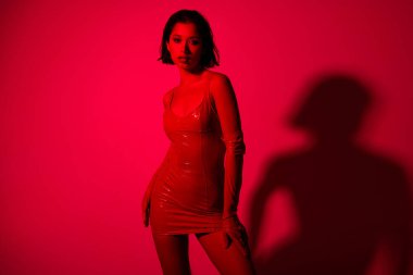 Çekici genç kadın, seksi manken kalçalarının fotoğrafı kırmızı neon ışıklı arka planda izole edilmiş kırmızı deri elbiseler giyer..