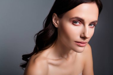 Kumral bukleli bir kadının yakın plan fotoğrafı. Kamera gri arkaplanı izole etmiş..